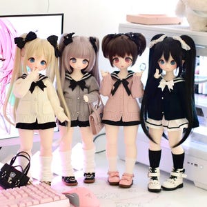 May include: Four dolls with long black hair, wearing sailor collars and sweaters, stand on a table with a pink keyboard and mouse. The dolls are wearing different coloured sweaters: white, grey, pink, and black.