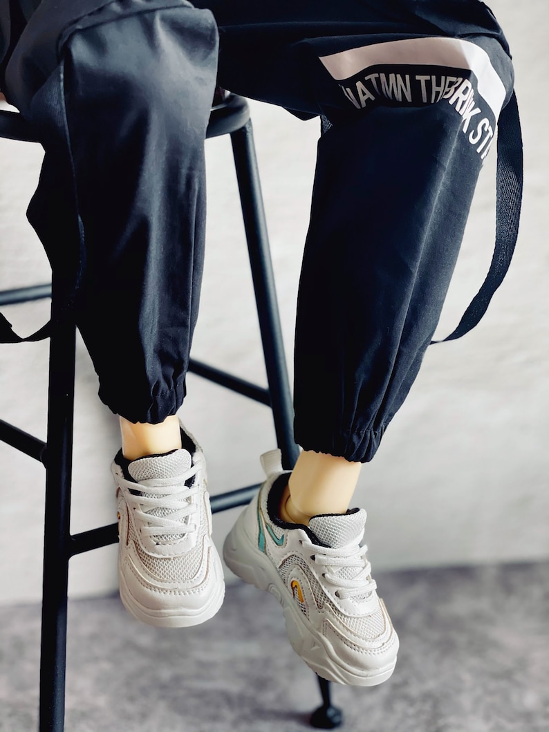 Puede incluir: Zapatillas blancas con detalles negros y dise&ntilde;o de malla. Las zapatillas tienen una suela gruesa y las lleva una persona que viste pantalones negros con una raya blanca y el texto "ATM THRK ST" en el lateral.