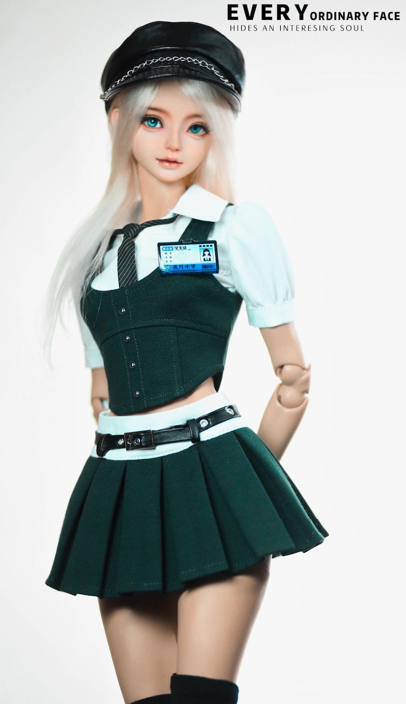 May include: A doll wearing a dark green school uniform with a pleated skirt, a white collared shirt, and a black tie. The doll has a black cap with a silver chain and a name tag. The text "EVERY ORDINARY FACE HIDES AN INTERESTING SOUL" is at the top.