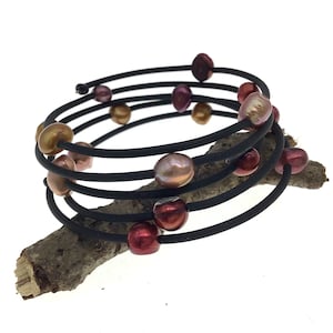 May include: A black wire bracelet with multiple strands and a variety of pearl-like beads in shades of pink, brown, and gold.
