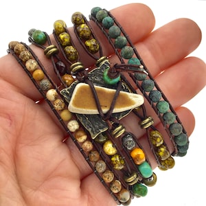 May include: A multi-strand bracelet with brown leather cord, turquoise, and brown, yellow, and white beads. The bracelet has a large, brown, ceramic pendant with a metal accent.