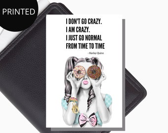 May include: A white card with a black and white illustration of a girl holding two doughnuts in front of her eyes. The text on the card reads "I don't go crazy. I am crazy. I just go normal from time to time - Harley Quinn."