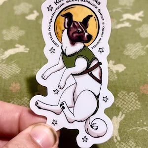 May include: A sticker featuring a dog in a green vest and harness, with text in Russian. The dog is white with brown and black markings, set against a yellow circle. The sticker has a white border and star accents.