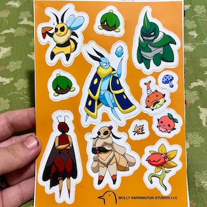 May include: A sheet of colorful stickers featuring various cartoon insects and creatures, including a bee, a moth, and a beetle. The stickers are on an orange background. The text "MOLLY HARRINGTON STUDIOS LLC" is printed at the bottom.