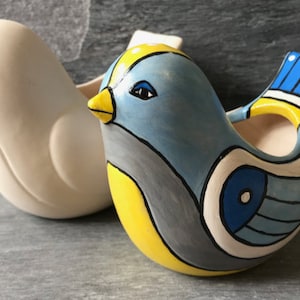 May include: Two ceramic bird planters, one white and one painted with blue, yellow and grey geometric patterns. The painted bird has a blue and white eye.