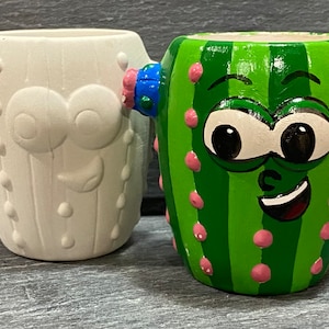 May include: Two ceramic cactus planters, one painted green with a smiling face and pink and blue accents, the other is unpainted white.