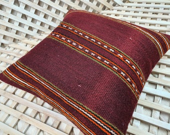 May include: A burgundy throw pillow with a woven pattern of orange, white, and green stripes. The pillow has a square shape and is made of a soft, textured fabric.