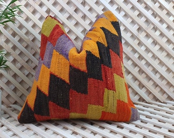 May include: A colorful, geometric patterned throw pillow with a mix of orange, red, yellow, black, and purple hues. The pillow is made of woven fabric and has a slightly textured surface.