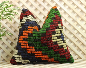 May include: A colorful patterned pillow with a geometric design in shades of black, green, orange, red, and white. The pillow is made of woven fabric and has a slightly textured surface.