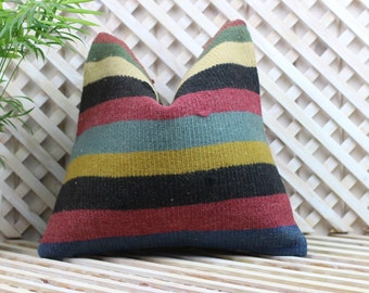 May include: A striped throw pillow with a colorful pattern of red, blue, yellow, and black stripes. The pillow is made of a woven fabric and has a slightly textured surface.