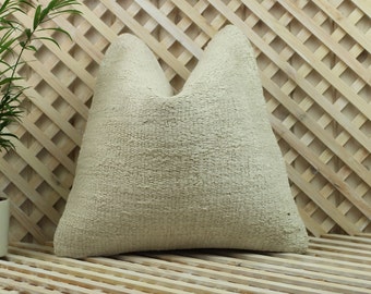 May include: A cream-colored throw pillow with a textured woven fabric. The pillow is sitting on a wooden slatted surface.