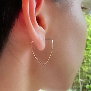 Könnte beinhalten: Ein Paar silberne Dreiecks-Creolen. Die Ohrringe werden am Ohr getragen.