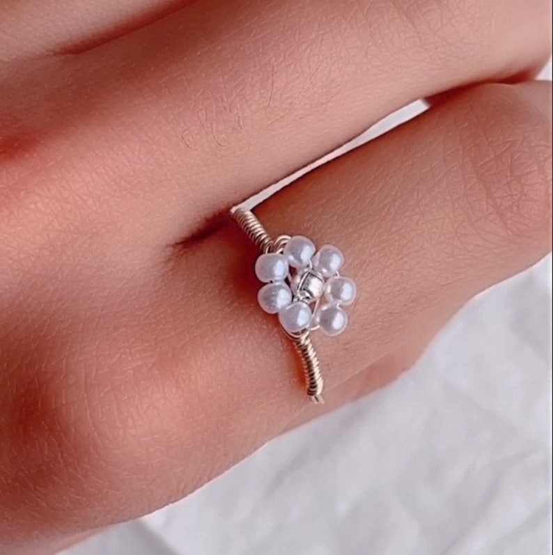 Puede incluir: Un anillo de alambre plateado con un dise&ntilde;o de flor de perlas blancas.