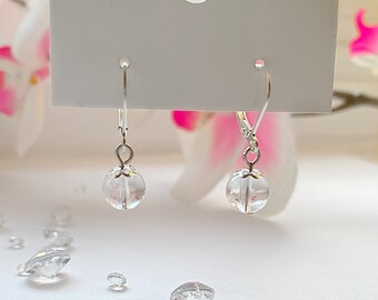 May include: A pair of silver earrings with clear crystal ball charms. The earrings have a simple design and are perfect for everyday wear.