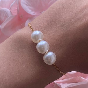 Könnte beinhalten: Ein zartes Armband aus einer goldenen Kette mit drei weißen Perlen. Die Perlen sind gleichmäßig verteilt und bilden ein klassisches und elegantes Design.