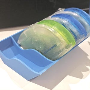May include: A light blue plastic organizer tray holding four adhesive tape runners. The runners have translucent, glittery covers in shades of lime green and blue, with the text Creative Memories printed on the green runner casing.