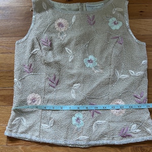 May include: Beige sleeveless top with floral embroidery in pink, blue, and white. The top features a textured fabric and a zipper closure in the back. The waist measures approximately 16 inches.