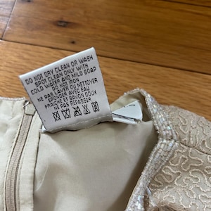 May include: Close-up of a cream-colored garment with a zipper and a tag. The tag reads "DO NOT DRY CLEAN OR WASH SPOT CLEAN ONLY WITH COLD WATER AND MILD SOAP DO NOT IRON NE PAS LAVER OU NETTOYER EPONGER AVEC EAU FRAICHE ET SAVON DOUX NE PAS REPASSER".