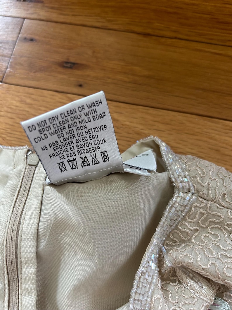 May include: Close-up of a cream-colored garment with a zipper and a tag. The tag reads "DO NOT DRY CLEAN OR WASH SPOT CLEAN ONLY WITH COLD WATER AND MILD SOAP DO NOT IRON NE PAS LAVER OU NETTOYER EPONGER AVEC EAU FRAICHE ET SAVON DOUX NE PAS REPASSER".