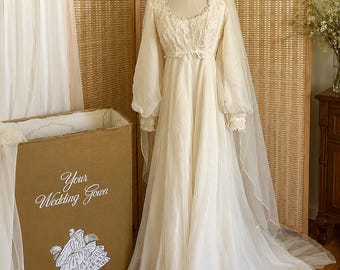 Puede incluir: Un vestido de novia color blanco roto con mangas largas tipo obispo, escote redondo y detalles de encaje intrincado en el corpiño. El vestido presenta una falda fluida y un velo a juego. Una caja de cartón marrón con la etiqueta "Your Wedding Gown" está cerca.