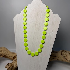 Puede incluir: Un collar que presenta una serie de discos circulares de color verde lima vibrante que se alternan con pequeñas cuentas esféricas pulidas de tono plateado. Las cuentas y los discos están dispuestos en una sola hebra, creando un patrón uniforme.