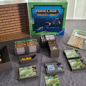 May include: A Minecraft Builders & Biomes board game set. The box is green with the game title and characters. The game includes various components like cards, wooden blocks, and game boards, all arranged on a gray surface.