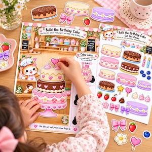 May include: A paper activity set titled Build the Birthday Cake featuring illustrated sheets with cut-out cake layers, frosting, bows, and fruit decorations. The set includes a scene of a bakery with a cartoon cat and instructions for assembling layered cakes.