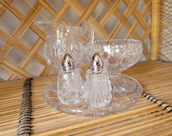 May include: A set of crystal salt and pepper shakers with silver tops, a crystal creamer, and a crystal bowl on a crystal tray.