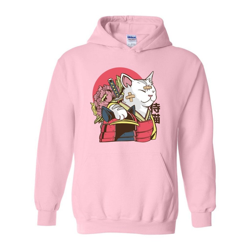 Peut inclure: Sweat-shirt &agrave; capuche rose avec un motif repr&eacute;sentant un chat blanc portant un casque de samoura&iuml; et tenant une &eacute;p&eacute;e. Le chat a des bandages sur le visage et le texte "侍猫" est imprim&eacute; sur le sweat-shirt.