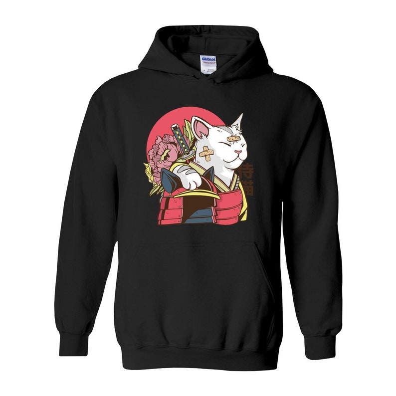 Peut inclure: Sweat-shirt &agrave; capuche noir avec un chat blanc portant une tenue de samoura&iuml; rouge et noire et tenant une &eacute;p&eacute;e. Le chat a des bandages sur le visage et une fleur rose derri&egrave;re lui. Le texte "侍猫" est imprim&eacute; sur le sweat-shirt.