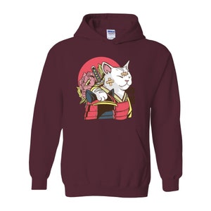 Peut inclure: Un sweat &agrave; capuche bordeaux avec un chat blanc portant un casque de samoura&iuml; et tenant une &eacute;p&eacute;e. Le chat a un bandage sur l'&oelig;il et une fleur derri&egrave;re lui.