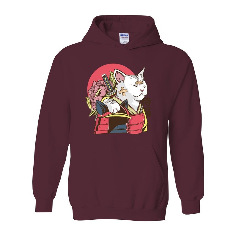 Peut inclure: Un sweat &agrave; capuche bordeaux avec un chat blanc portant un casque de samoura&iuml; et tenant une &eacute;p&eacute;e. Le chat a un bandage sur l'&oelig;il et une fleur derri&egrave;re lui.