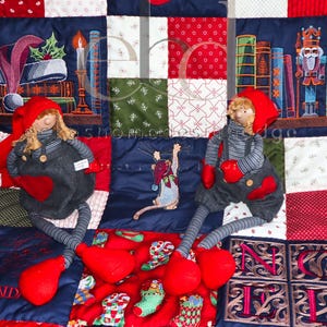 Könnte beinhalten: Eine Patchwork-Decke mit weihnachtlichen Stoffquadraten, die Strümpfe, Bücher, einen Nussknacker und eine Maus zeigen. Zwei Stoffpuppen mit roten Mützen, grauen Latzhosen und gestreiften Ärmeln sitzen auf der Decke, die den Schriftzug NOEL enthält.