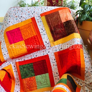 Peut inclure: Une courtepointe colorée avec des patchworks carrés dans les tons de rouge, orange, jaune et vert. La courtepointe présente des motifs matelassés complexes et est drapée sur une chaise. Le texte "Eckas Sewing Edge" est visible.