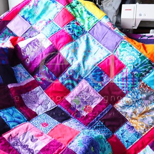 Può includere: Una trapunta patchwork composta da una varietà di blocchi di tessuto quadrati nelle tonalità magenta, viola, turchese e arancione. Il design include vari motivi, tra cui disegni floreali e illustrazioni dettagliate di gatti e farfalle.