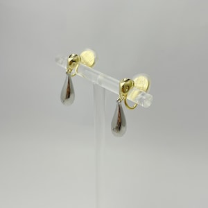 Könnte beinhalten: Ein Paar silberne Ohrringe in Tropfenform mit goldenen Akzenten. Die Ohrringe sind im Clip-Stil.