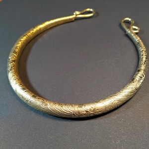 Peut inclure: Un collier ras du cou ouvert de couleur dorée, orné de motifs floraux et de feuilles complexes. Le collier est doté d'une fermeture à crochet à chaque extrémité. Le métal a un aspect texturé, et le motif est uniforme sur toute la pièce.
