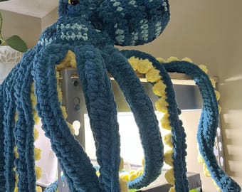 May include: A large, handmade crochet octopus plush toy featuring a dark teal and light blue striped head with shiny black eyes. The eight long, dangling tentacles are dark teal on the outside and lined with textured, bright yellow yarn suckers.