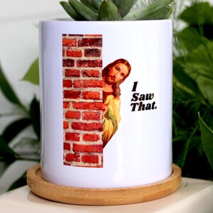 May include: White ceramic planter with a brick wall and a picture of Jesus peeking around the corner. The text "I Saw That." is printed on the planter.