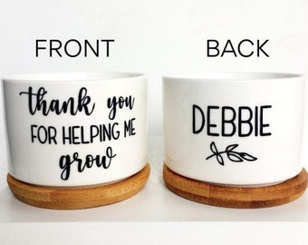 May include: White ceramic planter with a bamboo base. The front of the planter says "Thank you for helping me grow". The back of the planter says "Debbie" with a small leaf design.