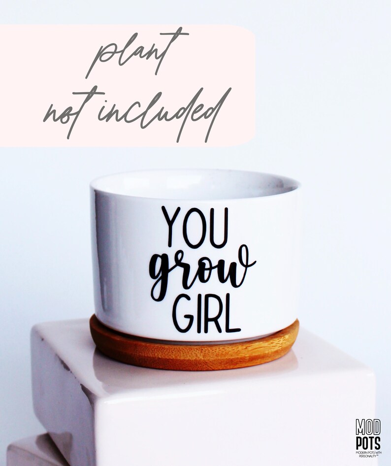 Puede incluir: Maceta de cer&aacute;mica blanca con base de madera. La maceta tiene texto negro que dice "You grow girl".