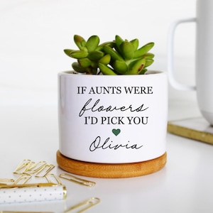 May include: A white ceramic cylindrical planter with a bamboo base containing a green succulent. The planter features black text that reads IF AUNTS WERE flowers I'D PICK YOU with a small green heart and the name Olivia printed below.