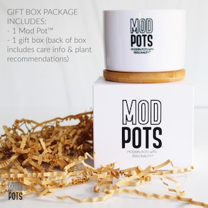 May include: A white ceramic Mod Pot with the brand's logo, sitting on a wooden coaster and a white box. The box also features the Mod Pots logo. The gift box package includes a Mod Pot and a gift box with care info and plant recommendations.