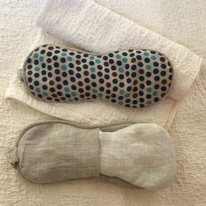 May include: Two eye masks, one with a blue and brown polka dot pattern and one plain light gray.