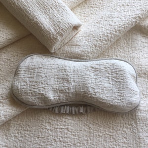 May include: A white eye mask with a ruffled edge and a textured fabric. The mask is lying on a white textured fabric.