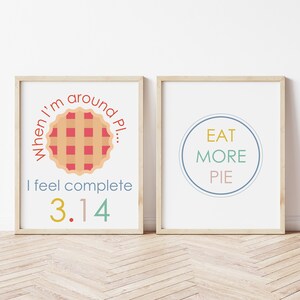 K&ouml;nnte beinhalten: Zwei gerahmte Drucke mit Kuchen-bezogenem Text. Der erste Druck zeigt einen roten und braunen Kuchen mit dem Text "When I'm around Pi... I feel complete 3.14". Der zweite Druck zeigt einen blauen Kreis mit dem Text "Eat More Pie" in Gelb, Gr&uuml;n und Rosa.
