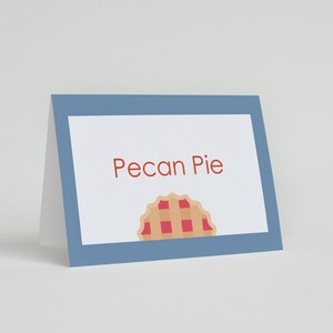 K&ouml;nnte beinhalten: Eine blaue Karte mit wei&szlig;em Rand und dem Text "Pecan Pie" in Rot. Unter dem Text befindet sich eine kleine Illustration einer Pecan-Torte mit roter F&uuml;llung.