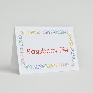 K&ouml;nnte beinhalten: Eine wei&szlig;e Karte mit dem Text "Raspberry Pie" in Rot. Die Karte ist von einem Rand aus bunten Zahlen umgeben.