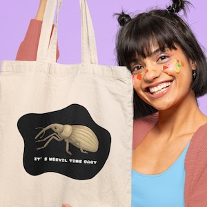 May include: A person holding a white tote bag with a black and white illustration of a weevil and the text "It's Weevil Time Baby".