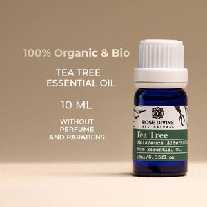 Könnte beinhalten: Eine blaue Glasflasche mit weißem Verschluss, die 10 ml Teebaumöl enthält. Die Flasche ist mit "Rose Divine All Natural Tea Tree (Melaleuca Alternifolia) Pure Essential Oil" beschriftet. Das Etikett gibt auch an, dass das Öl 100% biologisch und bio ist, ohne Parfum und Parabene.